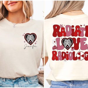 Op de afbeelding: Een wit T-shirt met een rode hartgrafiek met een gestileerde röntgenfoto van een ribbenkast. De tekst "Radiate Love Radiology" is in rode en roze letters op de achterkant van het shirt gedrukt. De naam "Jennifer" is onder de hartgrafiek op de voorkant van het shirt gedrukt.