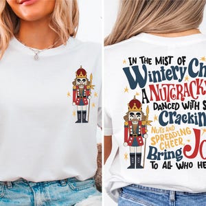 May include: White t-shirt with a Nutcracker illustration on the left side and the text "IN THE MIST OF Wintery Chill A NUTCRACKER DANCED WITH SKILL Cracking NUTS AND SPREADING CHEER Bring JOY TO ALL WHO HEAR" on the right side.
