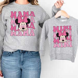 a woman wearing a mickey mouse sweatshirt and a minnie mouse sweatshirt