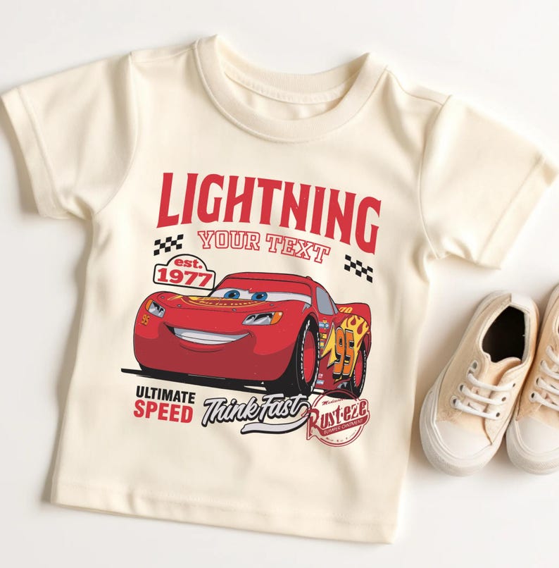 A white t-shirt with a red and black design featuring a red car and the text "Lightning YOUR text est. 1977" and "Ultimate SPEED Think fast Rust-o-zebra". The t-shirt is placed next to a pair of white sneakers.