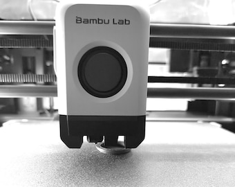 Op de afbeelding: Een close-up van een witte 3D-printermondstuk met de tekst "Bambu Lab" erop gedrukt. Het mondstuk is boven een wit oppervlak geplaatst.