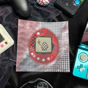 Könnte beinhalten: Ein rotes digitales Haustierspiel mit einem pixeligen Charakter auf dem Bildschirm. Das Spiel befindet sich in einer transparenten Plastiktüte mit einem Rastermuster. Weitere elektronische Geräte, darunter eine Spielkonsole und ein Handheld-Spiel, befinden sich im Hintergrund.