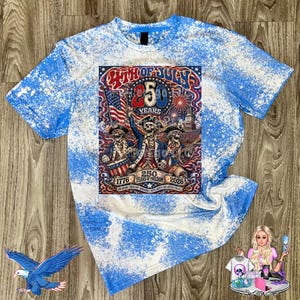 K&ouml;nnte beinhalten: Ein blau-wei&szlig;es, mit Bleichmittel gef&auml;rbtes T-Shirt mit einer Grafik von drei Skeletten in Kolonialkleidung, einer amerikanischen Flagge, Feuerwerk und dem Text 4TH OF JULY 250 YEARS 1776 2026 ONE NATION UNDER GOD INDIVISIBLE WITH LIBERTY AND JUSTICE FOR ALL.