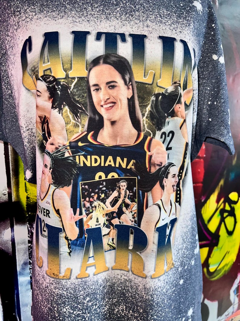 Puede incluir: Una camiseta azul y dorada con un aspecto desgastado que presenta un collage de im&aacute;genes de una jugadora de baloncesto. El nombre de la jugadora, "Caitlin Clark", est&aacute; escrito en letras doradas grandes en la parte superior de la camiseta. La camiseta tambi&eacute;n presenta las palabras "Indiana" y "22".