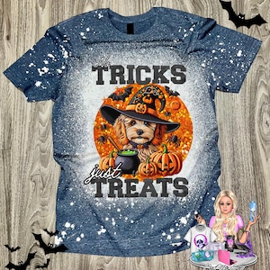May include: A blue t-shirt with a distressed white splatter effect. The shirt features a Halloween-themed graphic of a dog wearing a witch hat, surrounded by pumpkins, bats, and the text "No Tricks Just Treats."