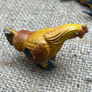 K&ouml;nnte beinhalten: Handbemalte H&uuml;hnerfigur im Vintage-Stil. Das Huhn ist &uuml;berwiegend gelb mit braunen und schwarzen Akzenten. Es hat einen roten Kamm und Kehllappen. Die Figur steht vor einem Jutegrund, was auf ein rustikales oder Bauernhaus-Thema hindeutet.