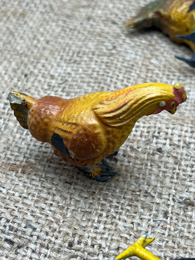 K&ouml;nnte beinhalten: Handbemalte H&uuml;hnerfigur im Vintage-Stil. Das Huhn ist &uuml;berwiegend gelb mit braunen und schwarzen Akzenten. Es hat einen roten Kamm und Kehllappen. Die Figur steht vor einem Jutegrund, was auf ein rustikales oder Bauernhaus-Thema hindeutet.