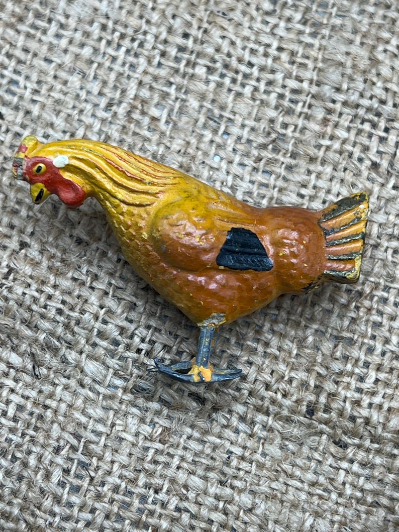 K&ouml;nnte beinhalten: Eine bemalte Metall-H&uuml;hnerfigur. Das Huhn hat einen gelben Kopf und Hals, einen braunen K&ouml;rper mit einer schwarzen Markierung und einen goldenen Schwanz. Die Figur steht auf zwei d&uuml;nnen Beinen.