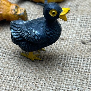 K&ouml;nnte beinhalten: Eine kleine, schwarze Vogelfigur mit gelbem Schnabel und F&uuml;&szlig;en. Der Vogel hat gelbe Augen und steht auf einer strukturierten Oberfl&auml;che. Weitere Vogelfiguren sind im Hintergrund zu sehen.