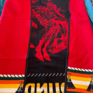 Puede incluir: Una manta roja y negra con un dise&ntilde;o nativo americano. La manta presenta un panel central negro con una ilustraci&oacute;n roja y la palabra "PENDLE" en amarillo. Los bordes tienen patrones de rayas con dise&ntilde;os de tipi.