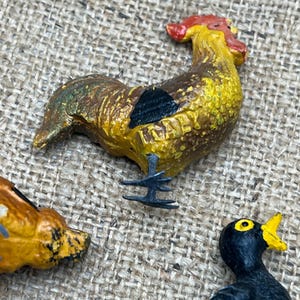 K&ouml;nnte beinhalten: Nahaufnahme einer bunten Hahnenfigur mit rotem Kamm, gelbem K&ouml;rper und braunen und schwarzen Akzenten. Das Wort "ITALY" ist auf der Figur zu sehen. Der Hahn ist Teil einer Sammlung von Tierfiguren.