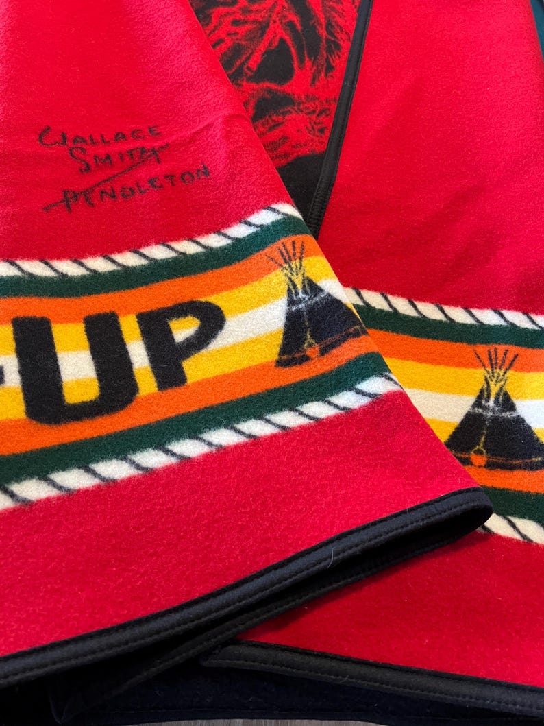 Puede incluir: Manta de lana roja con borde negro y dise&ntilde;o de rayas coloridas. La manta presenta la palabra "UP" en letras amarillas grandes, un gr&aacute;fico de tipi y el texto "Wallace Smith Pendleton".