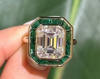 May include: A gold ring with a large emerald-cut diamond surrounded by a halo of smaller emerald-cut green gemstones.
