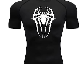 May include: Black compression top with a white spider-like design on the front. The short-sleeved top has a crew neck and is made of a stretchy material. The graphic is a stylized, symmetrical design with sharp, pointed elements.