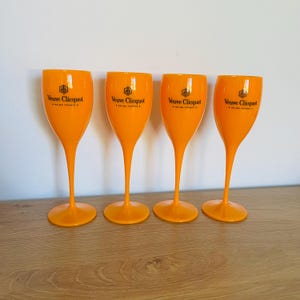 May include: Four orange plastic champagne flutes with the Veuve Clicquot logo printed on the front.