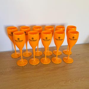 May include: Twelve orange plastic champagne flutes with the Veuve Clicquot logo printed on them.