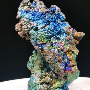 Könnte beinhalten: Ein Mineralspezimen mit botryoidaler, blasiger Textur und einer lebhaft irisierenden Oberfläche. Die Farben wechseln zwischen metallischem Blau, Grün, Gold und Violett über die abgerundeten, gehäuften Formationen der kristallinen Struktur.