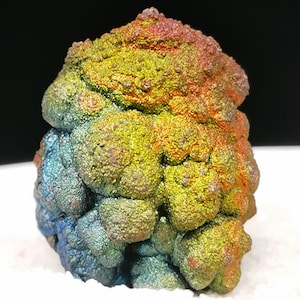 Könnte beinhalten: Ein botryoidales Mineralexemplar mit einer texturierten, abgerundeten Oberfläche und einem lebendigen, irisierenden Finish. Die Farben verlaufen über das Cluster und zeigen metallische Blau-, Grün-, Gelb-, Orange- und Rottöne.