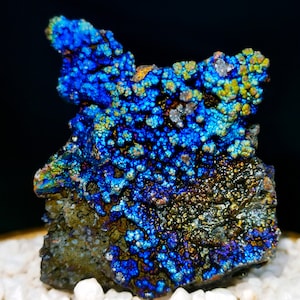 Könnte beinhalten: Nahaufnahme eines dunkelgrauen, irisierenden Steins mit blauem und grünem Schimmer. Der Stein hat eine raue, strukturierte Oberfläche und ist mit kleinen, runden Noppen bedeckt.