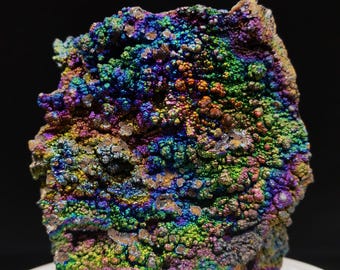 Könnte beinhalten: Ein großer, schillernder, mehrfarbiger Stein mit einer rauen, strukturierten Oberfläche. Der Stein ist mit kleinen, runden Noppen bedeckt und hat eine Vielzahl von Farben, darunter Blau, Grün, Lila und Gold.