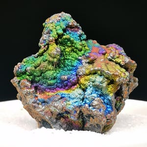 Könnte beinhalten: Ein rohes Mineralexemplar mit einer botryoidalen, blasigen Textur und einer lebendigen, irisierenden metallischen Oberfläche. Die Oberfläche zeigt ein Farbspektrum mit leuchtendem Grün, tiefem Blau, Gelb und Violett, was einen bunten Effekt erzeugt.