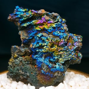 Könnte beinhalten: Ein großer, irisierender, dunkelgrauer Stein mit einer rauen, strukturierten Oberfläche. Der Stein hat einen Regenbogen-Schimmer mit Blautönen, Grüntönen, Violetttönen und Goldtönen.