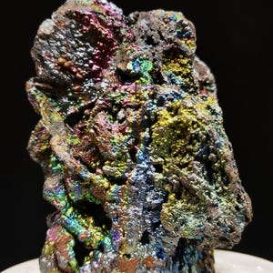 Könnte beinhalten: Nahaufnahme einer Mineralprobe mit rauer, strukturierter Oberfläche. Das Mineral zeigt eine lebendige Farbpalette, darunter schillernde Blau-, Grün-, Gelb- und Rottöne. Die Gesamtform ist unregelmäßig und felsig, mit dunklem Hintergrund.