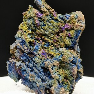 Puede incluir: Primer plano de un espécimen mineral con una superficie rugosa y texturizada. La roca muestra una vibrante gama de colores, incluyendo azules, verdes, amarillos y morados. La superficie del mineral tiene una apariencia cristalina, con un fondo oscuro.