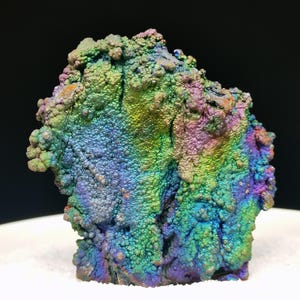 Könnte beinhalten: Ein Mineralexemplar mit einer botryoidalen, irisierenden Oberfläche, die ein lebendiges Farbspektrum aus metallischem Grün, Blau, Violett und Gold zeigt. Die Struktur weist eine unebene, texturierte Oberfläche mit tiefen Spalten auf.