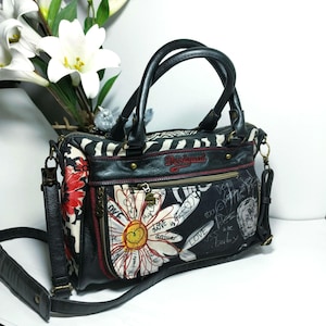 May include: Black handbag with a floral and zebra print design. The bag features a large daisy graphic, the words "love is the answer", and a black shoulder strap. The bag has black handles and a zip closure.