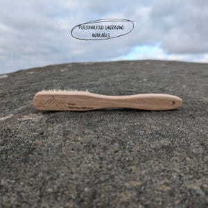 May include: A wooden brush with natural bristles, engraved with a mountain range and the text "Megan Think big, climb more".