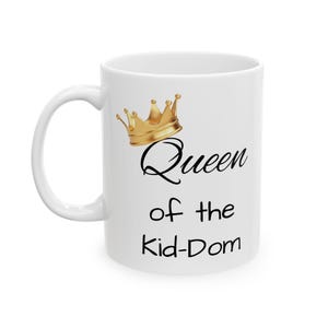 Pode incluir: Caneca de cerâmica branca com uma coroa dourada e o texto "Queen of the Kid-Dom" impresso nela.