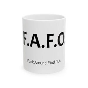 May include: White ceramic mug with the letters "F.A.F.O." in bold black font. Below the letters, the phrase "Fuck.Around.Find.Out." is printed in a smaller, black font. The mug is cylindrical and has a handle.