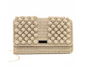 May include: A beige crocheted clutch bag with a gold chain strap and a gold metal clasp. The bag has a textured, bubble-like design.
