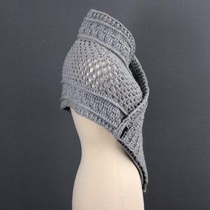 May include: Gray crochet shawl with a lacy pattern and a textured border. The shawl is draped over a mannequin.