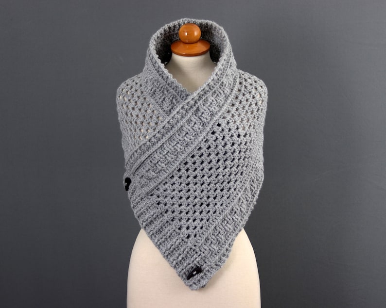 May include: Gray crocheted cowl with a triangular shape and a button closure. The cowl is made with a delicate open stitch pattern.