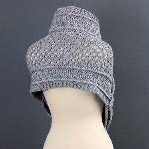 May include: A gray crocheted shawl with a geometric pattern. The shawl is draped over a mannequin.