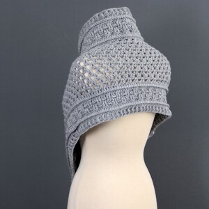May include: A gray crocheted shawl with a delicate openwork pattern. The shawl is draped over a dress form.