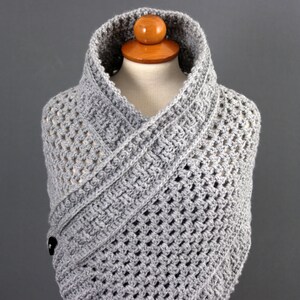 May include: Gray crocheted shawl with a button closure. The shawl is draped over a mannequin and has a wide, open collar.