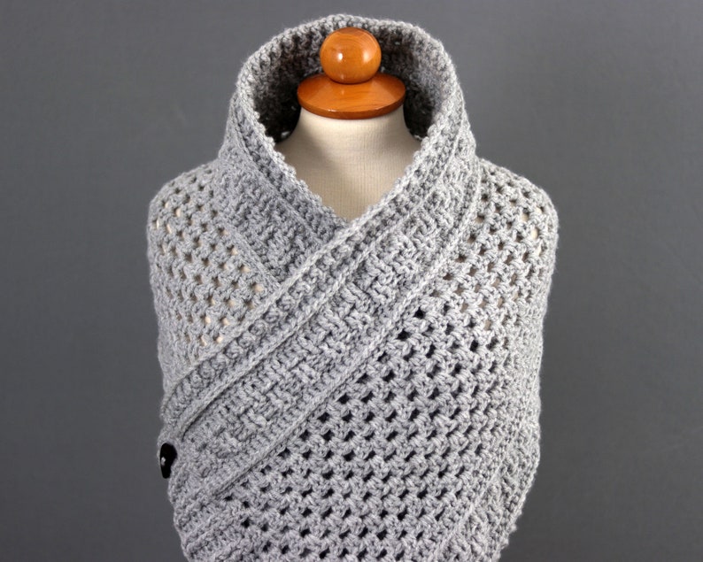 May include: Gray crocheted shawl with a button closure. The shawl is draped over a mannequin and has a wide, open collar.