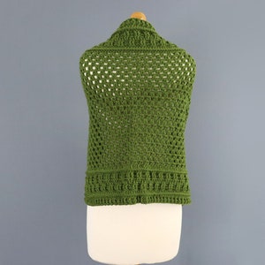 May include: A green crochet vest with a square stitch pattern. The vest is sleeveless and has a wide, open neckline.