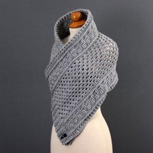May include: Gray crocheted shawl with a triangular shape and a textured pattern. The shawl is displayed on a mannequin.