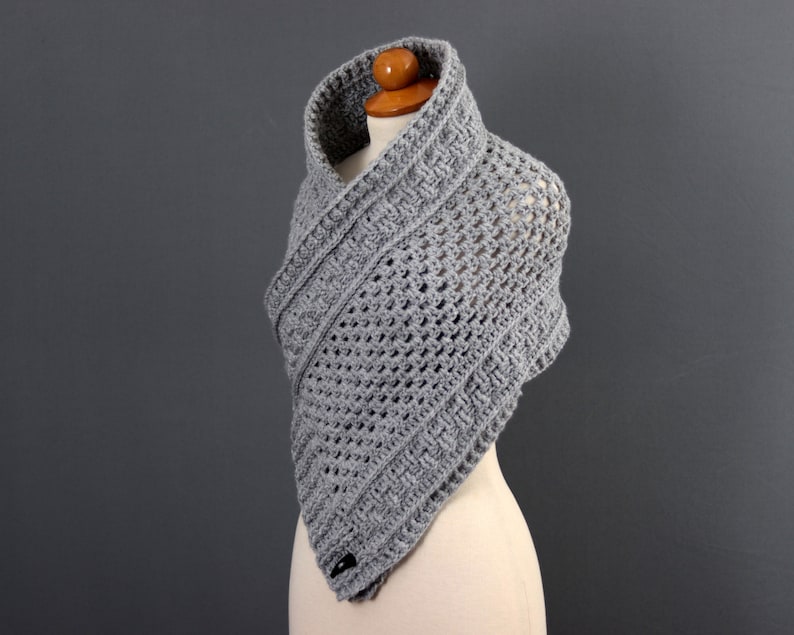 May include: Gray crocheted shawl with a triangular shape and a textured pattern. The shawl is displayed on a mannequin.