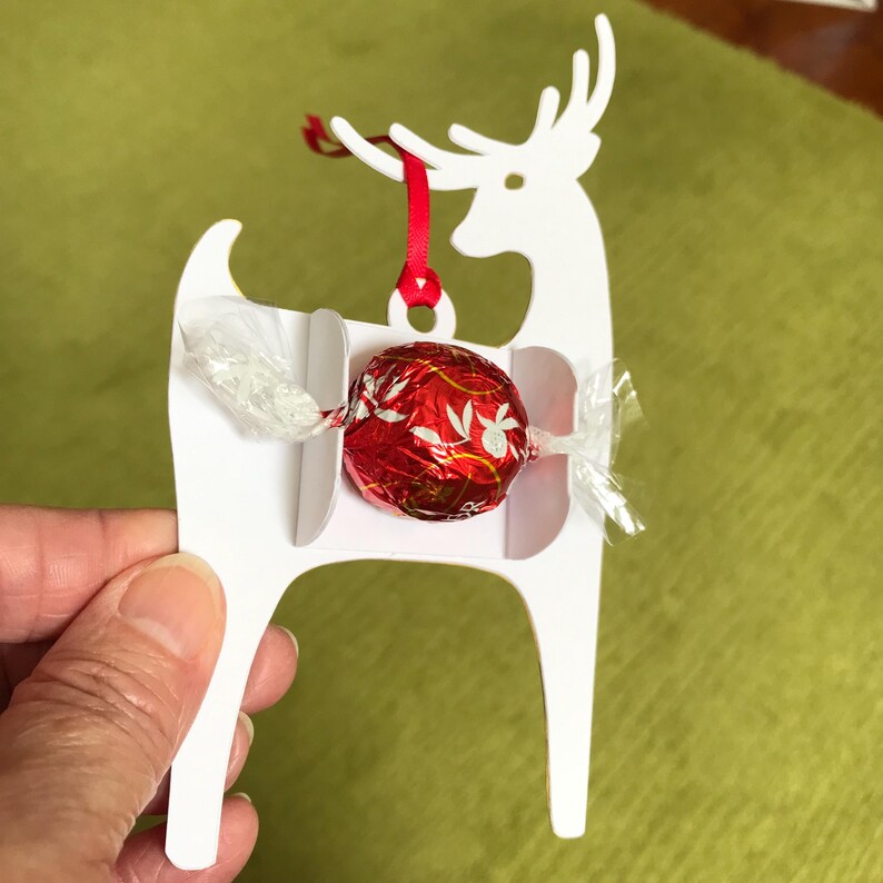 May include: White cardboard reindeer ornament with a red ribbon and a red and white chocolate candy inside.