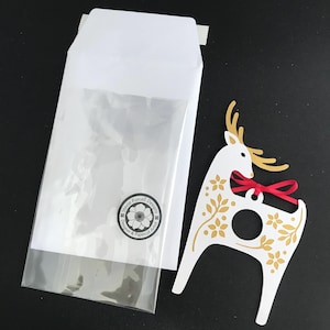 May include: A white paper reindeer ornament with gold floral details and a red ribbon. The ornament has a hole in the center for hanging.