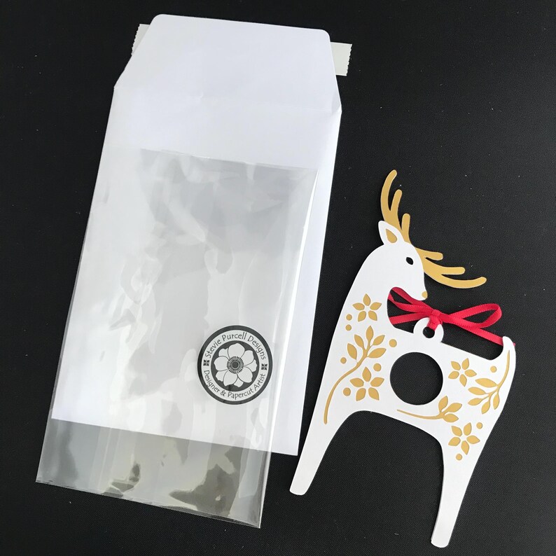 May include: A white paper reindeer ornament with gold floral details and a red ribbon. The ornament has a hole in the center for hanging.