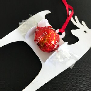 May include: White paper reindeer ornament with a red ribbon and a Lindor chocolate truffle in the sleigh.