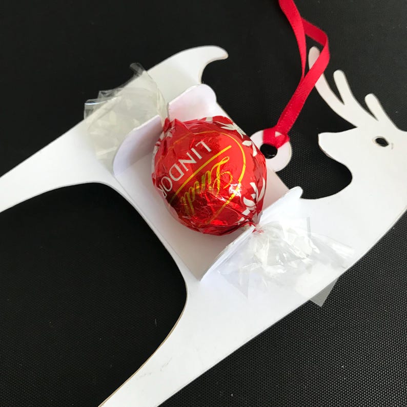 May include: White paper reindeer ornament with a red ribbon and a Lindor chocolate truffle in the sleigh.