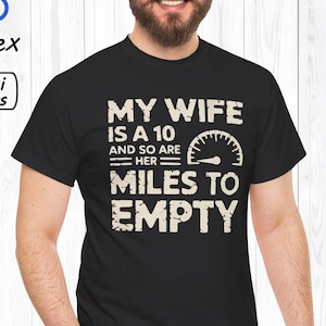 May include: Black t-shirt with a white graphic that reads "My wife is a 10 and so are her miles to empty". The graphic includes a speedometer with a needle pointing to the 10.