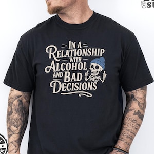 May include: Black t-shirt featuring the phrase "IN A RELATIONSHIP WITH ALCOHOL AND BAD DECISIONS". The design includes a skeleton wearing a blue beanie. The shirt also has an "ORIGINAL ARTWORK" logo.